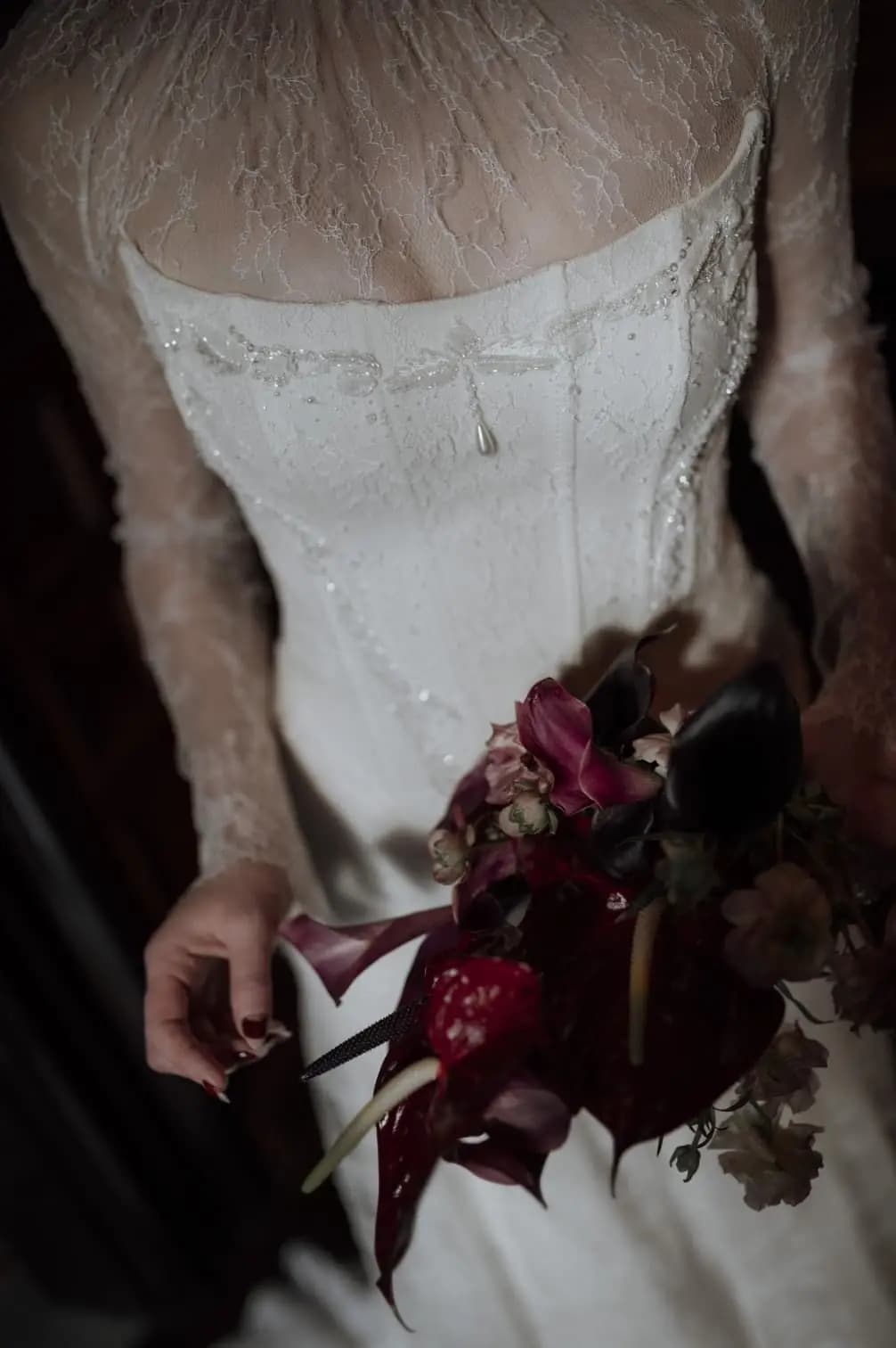 Close view of a lace wedding bodice and dark bouquet.
