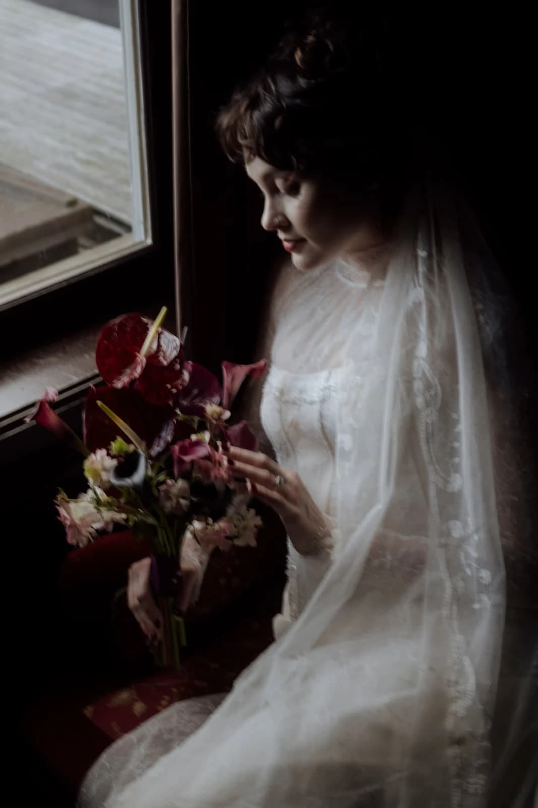 Bride holding a bouquet beside a window.