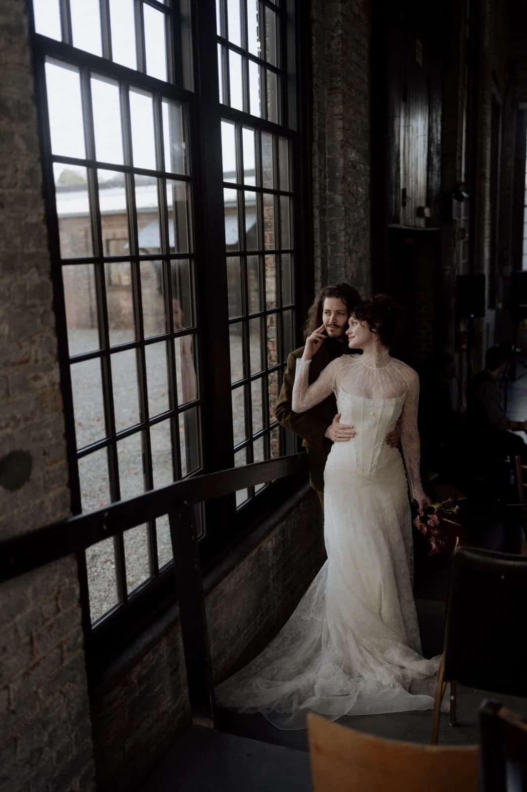 Bride and groom standing beside tall windows.