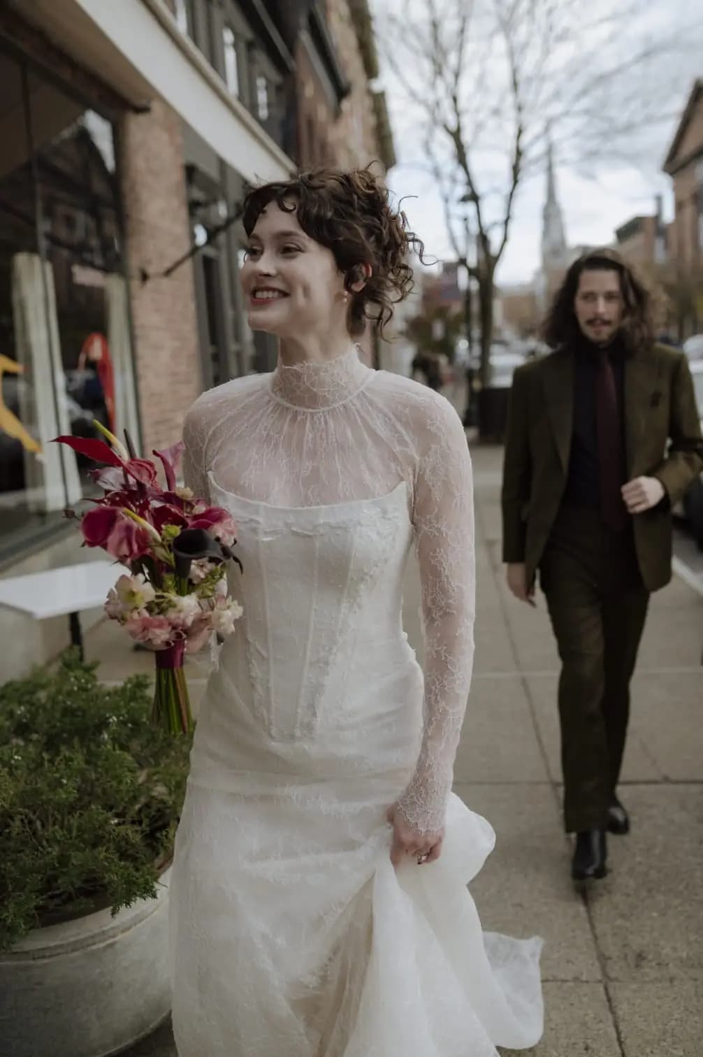 Bride carrying a bouquet on a city sidewalk.