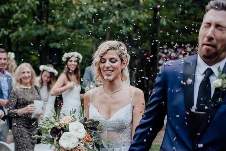 Bride walking with the groom as flower petals fall in a garden.