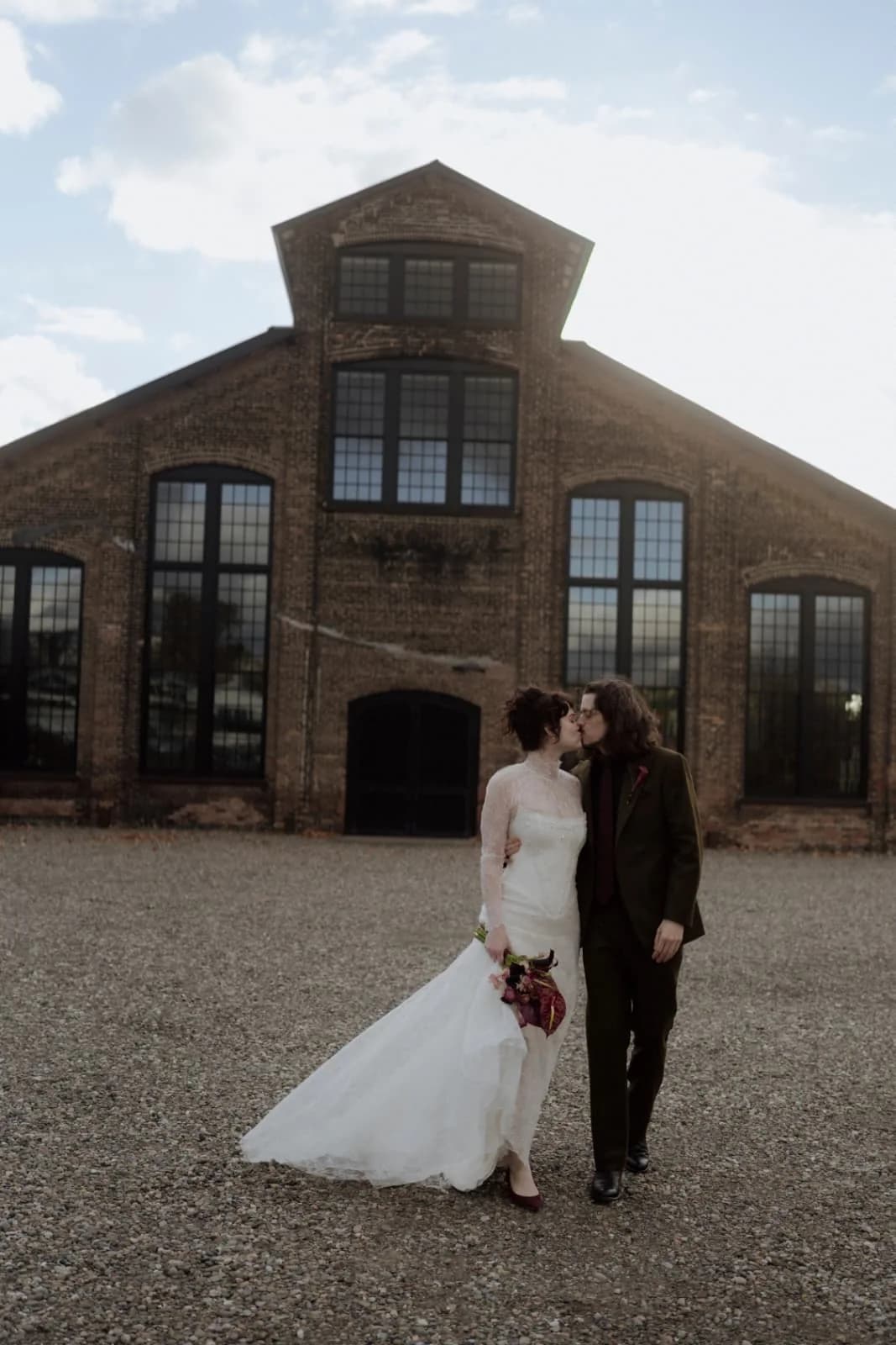 Bride and groom kissing outside a brick building.