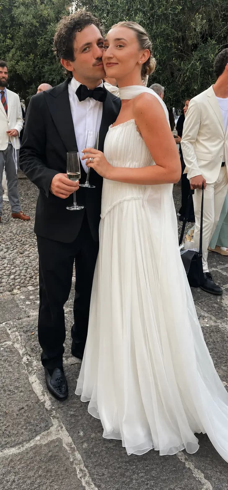 Bride and groom leaning together with champagne outdoors.