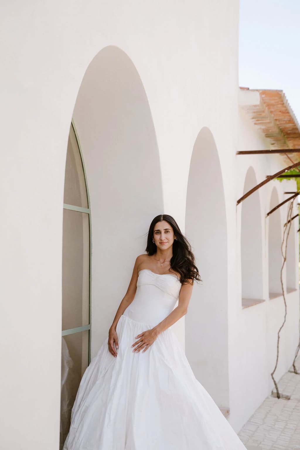 Bride in a strapless gown beside a white arched building.