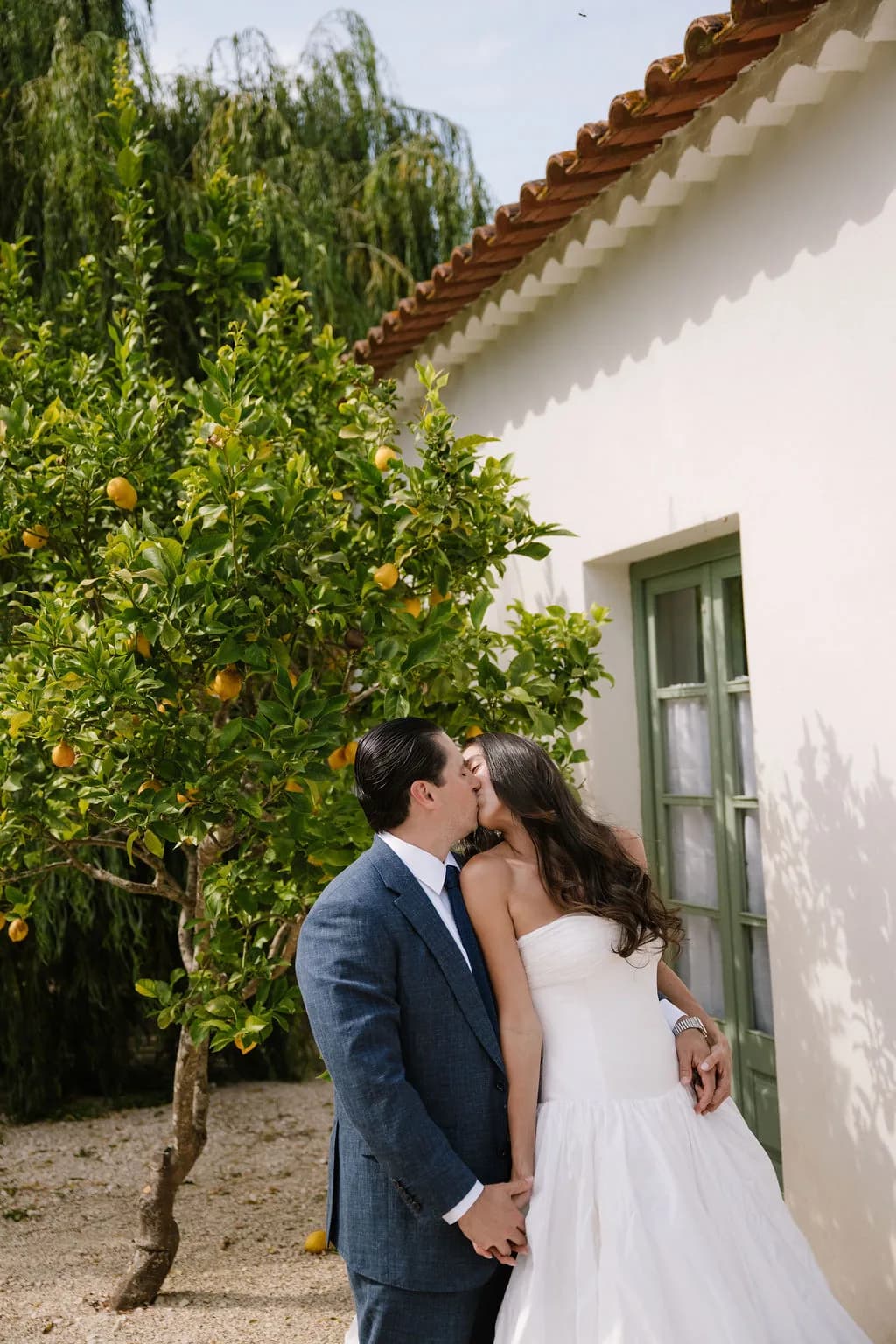 Bride and groom kissing beside a lemon tree and white house.