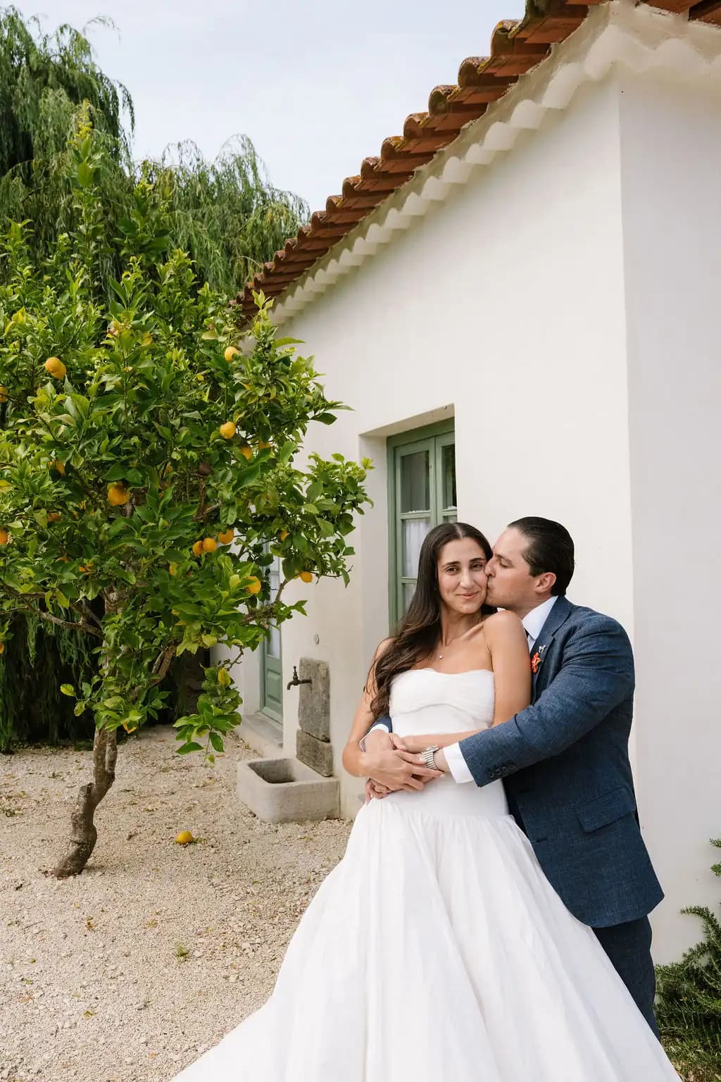 Bride and groom embracing beside a lemon tree.