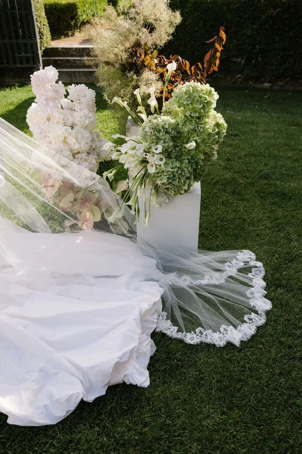 White wedding dress and floral arrangements laid on garden grass.