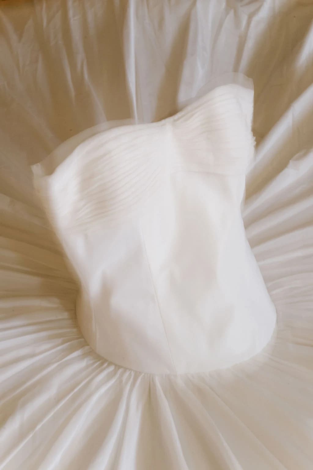 Close view of a pleated white wedding skirt on a bed.