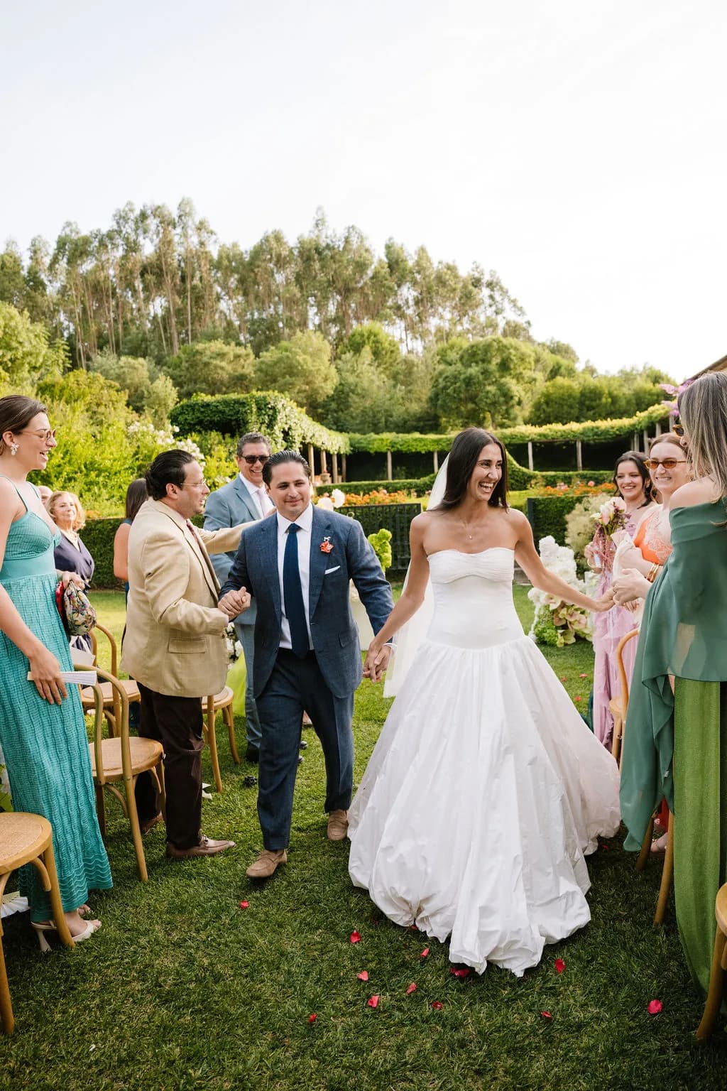 Bride and groom walking between guests on a garden lawn.