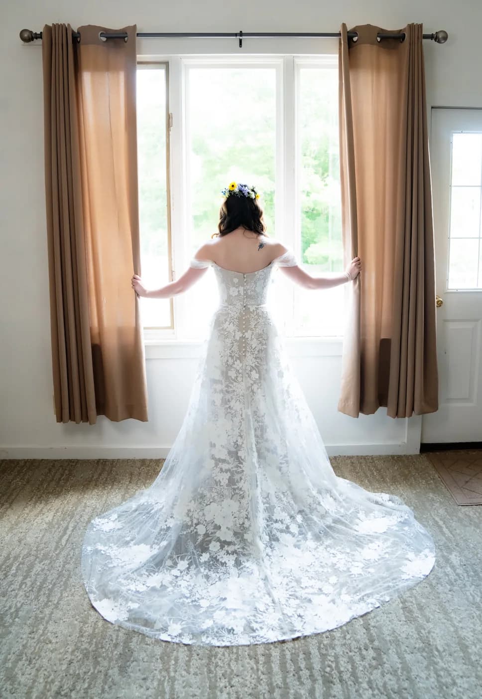 Bride viewed from behind at a bright window in a lace gown.