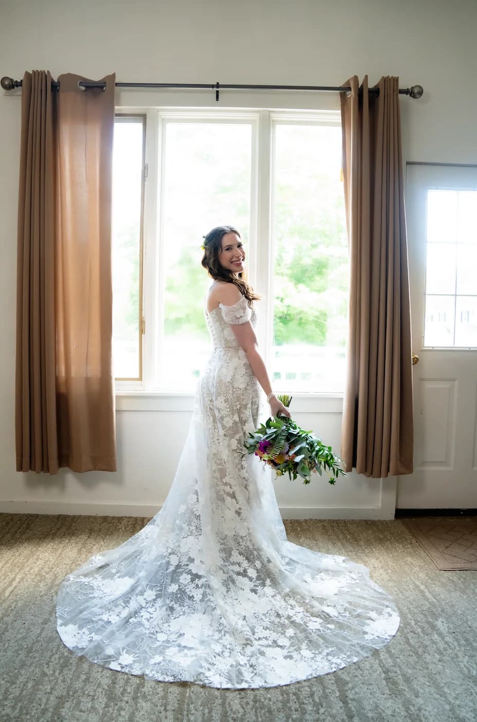 Bride posing by a window with a bouquet and lace train.