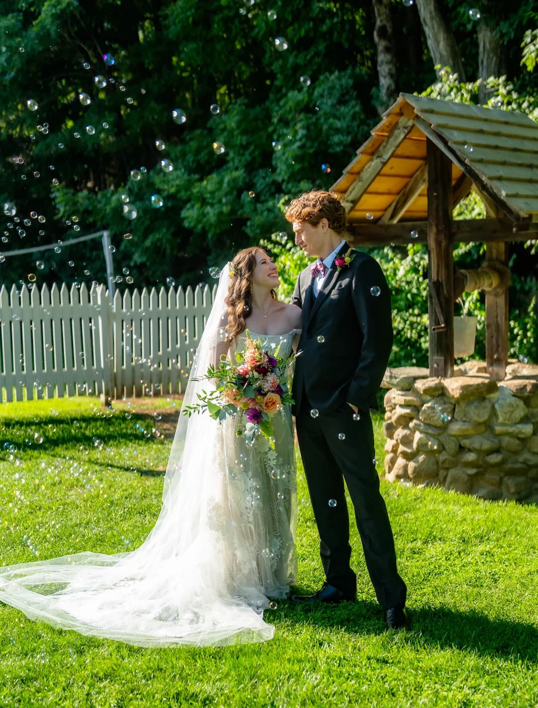 Bride and groom posing in a garden surrounded by bubbles.