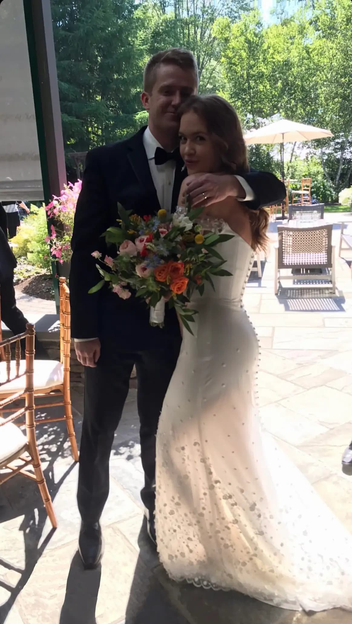 Bride and groom posing outdoors with a colorful bouquet.