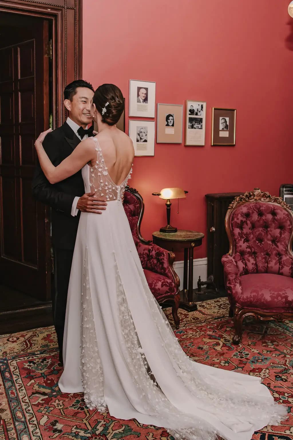 Bride and groom embracing in a room with red walls.