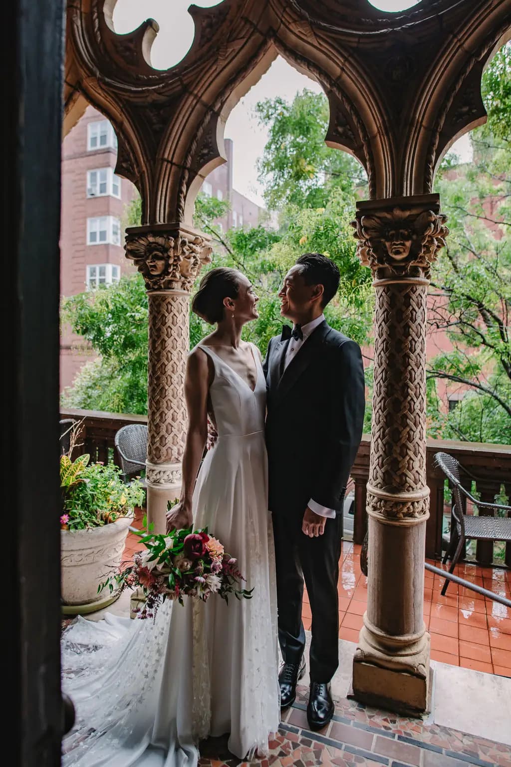 Bride and groom standing beneath ornate balcony arches.
