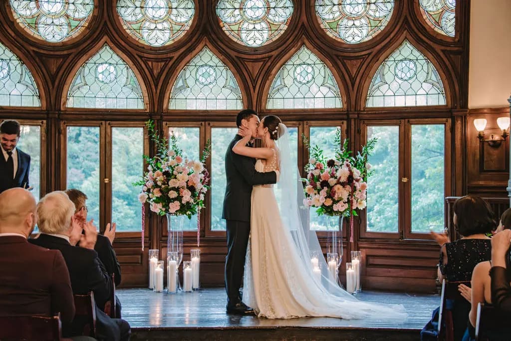 Bride and groom kissing during a ceremony before floral displays.