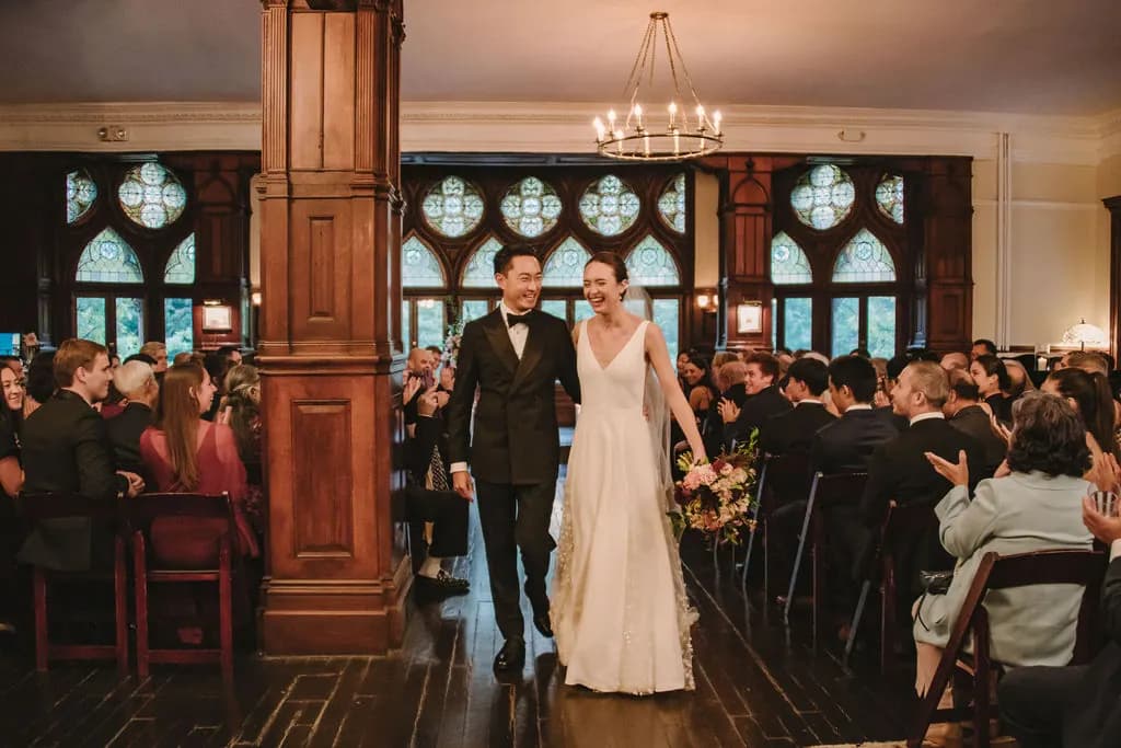 Bride and groom walking down the aisle between seated guests.