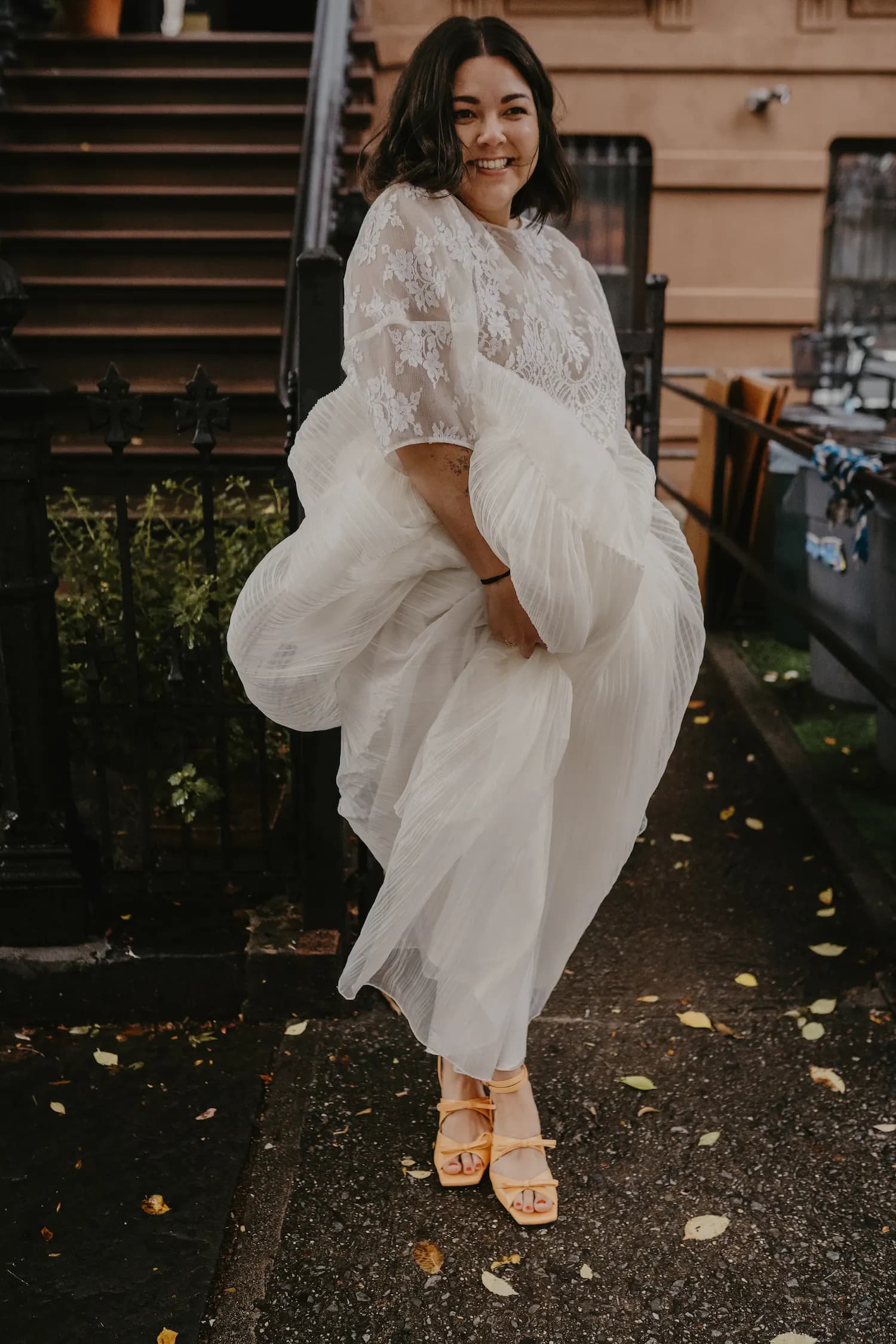 Smiling bride in a pleated gown outside a townhouse.