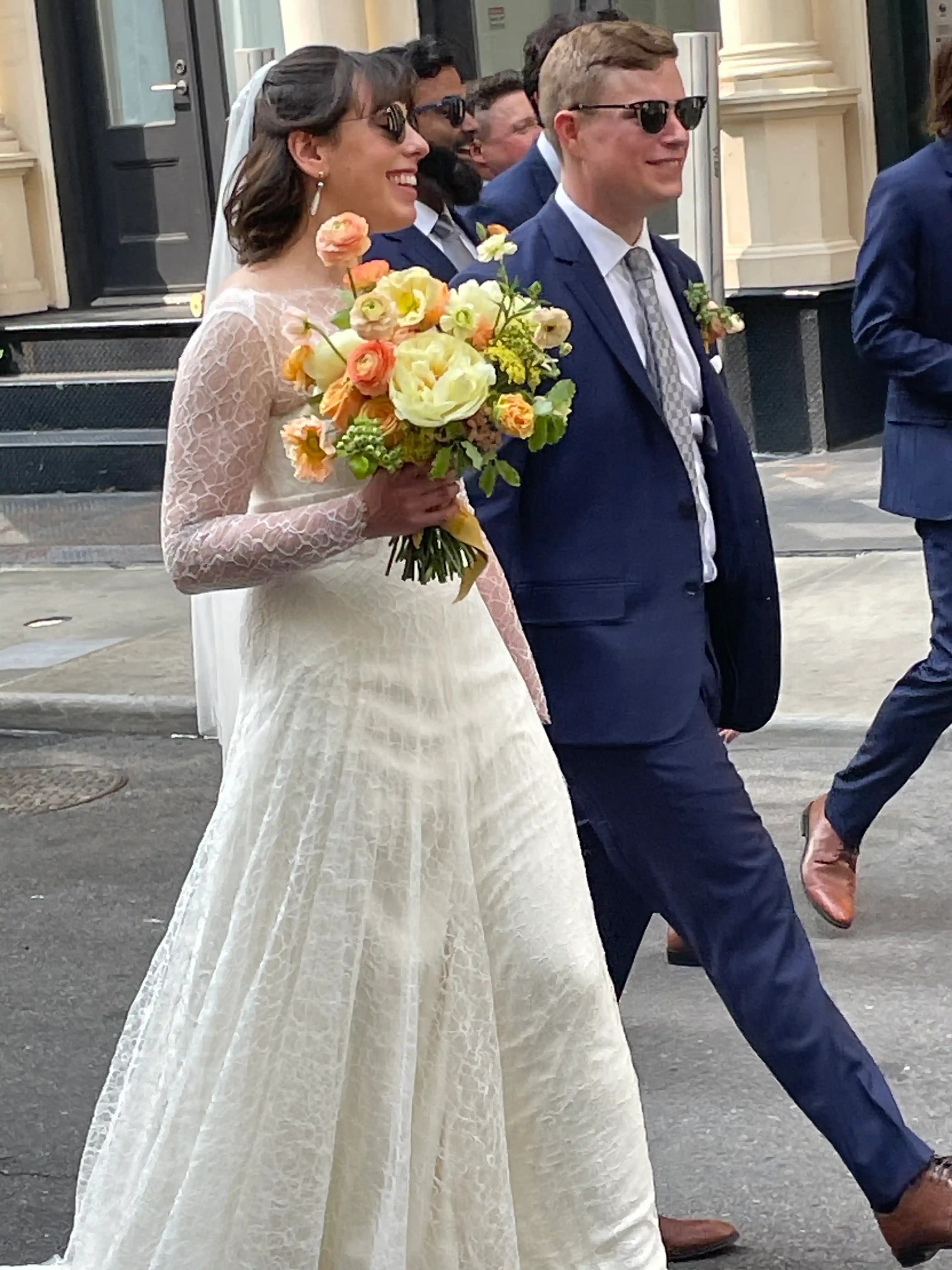 Bride and groom walking outdoors with a large flower bouquet.