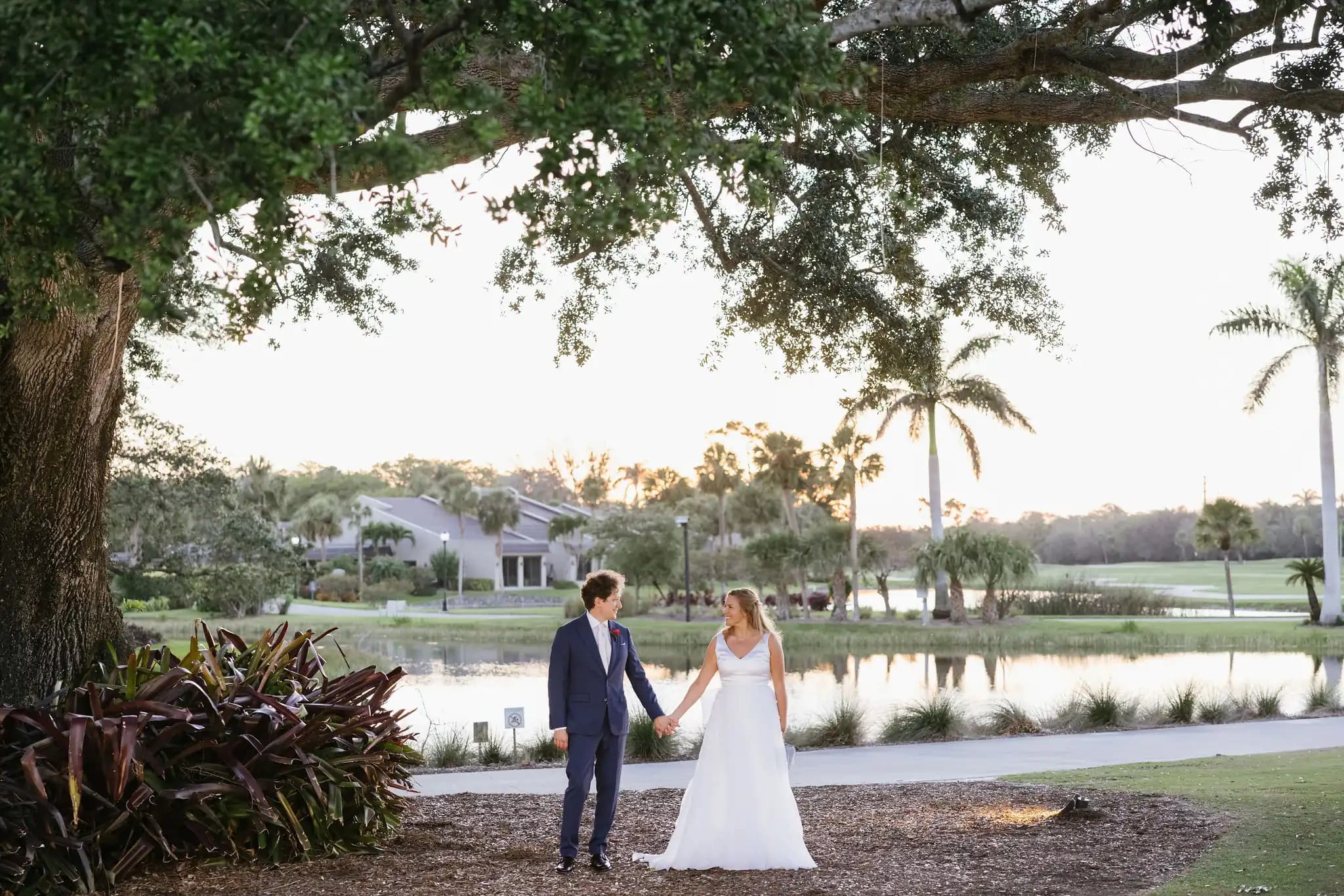 Bride and groom holding hands beside a pond at sunset.