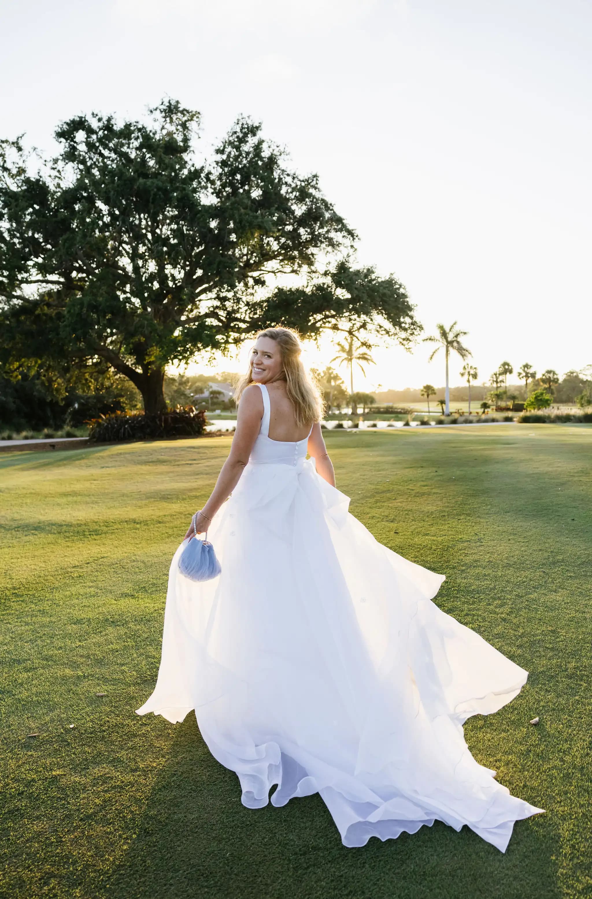 Bride looking back across a lawn at sunset.