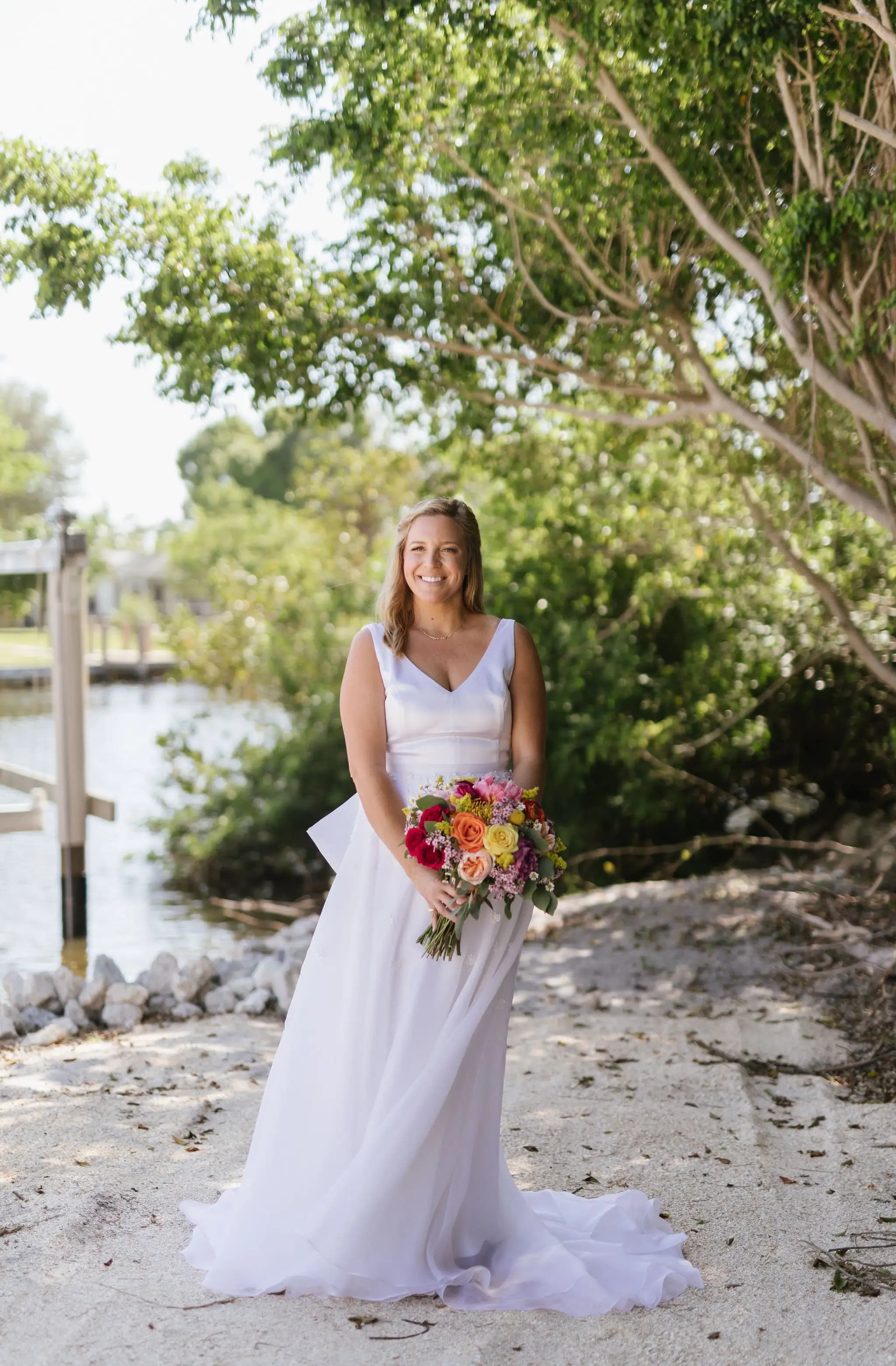 Bride holding a colorful bouquet beside the water.