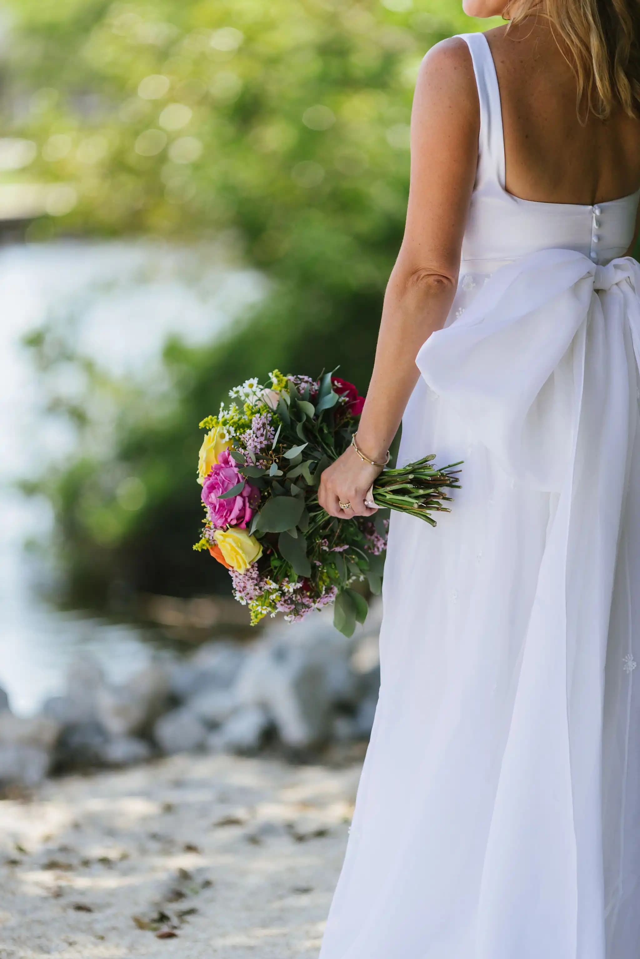 Close view from behind of a bride holding a bouquet by the water.