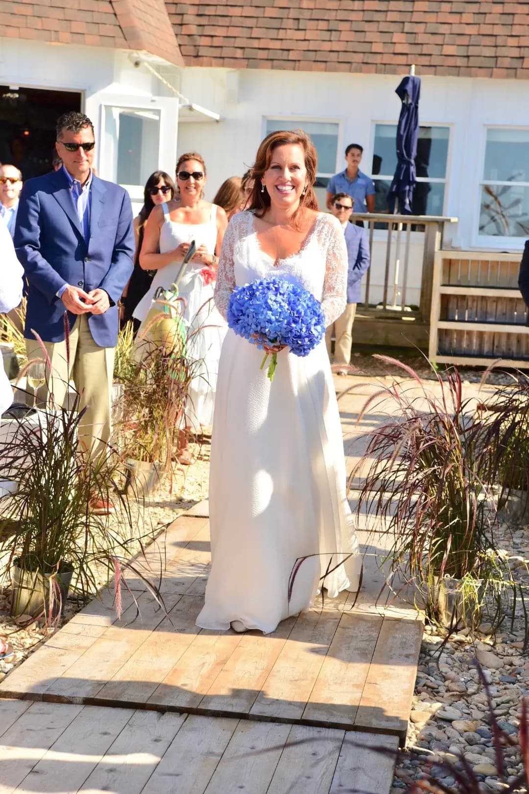 Bride holding blue hydrangeas on a sunny outdoor walkway.