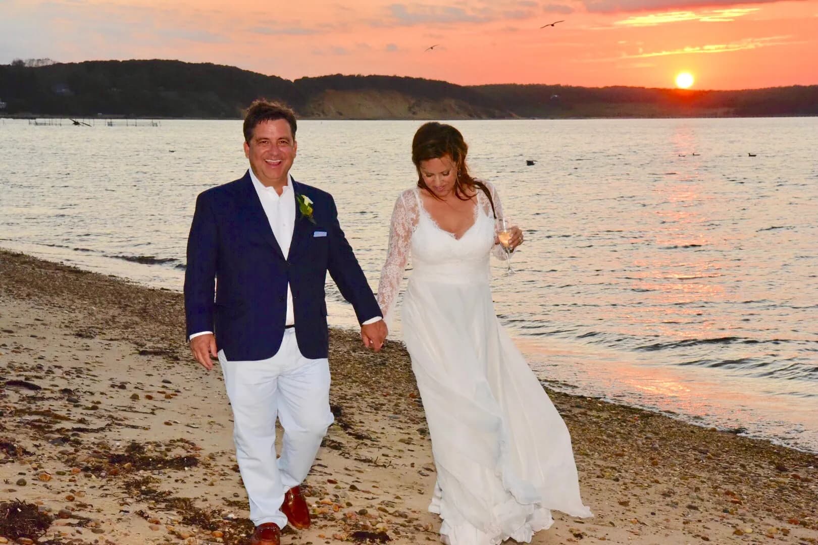 Bride and groom walking along a beach at sunset.