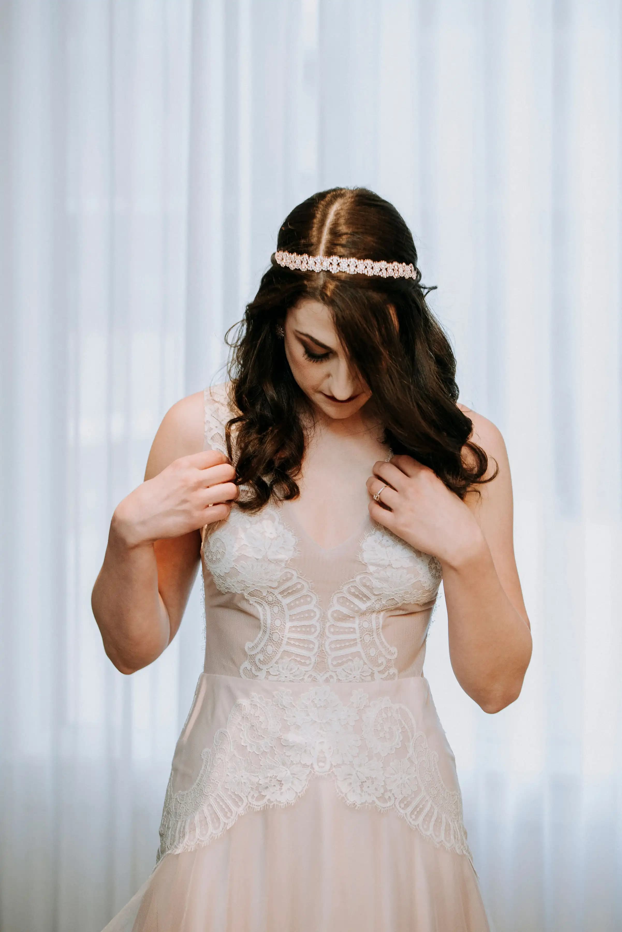 Close portrait of a bride adjusting a lace bodice and jeweled headband.