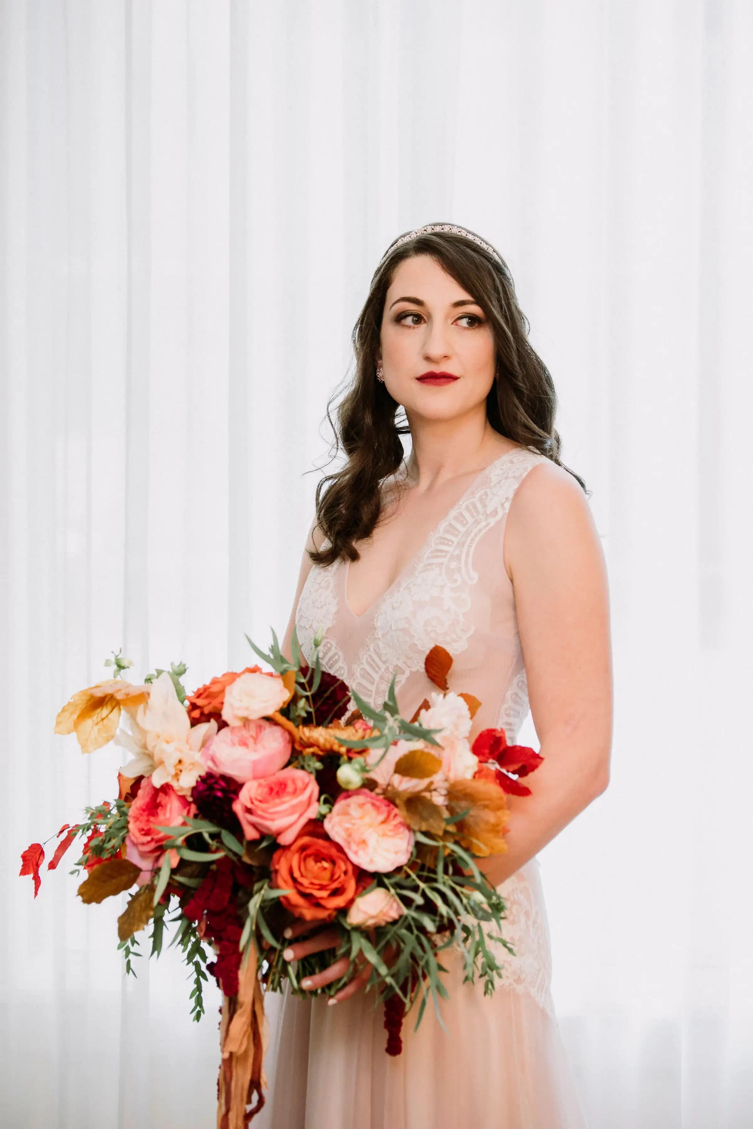 Bride holding a colorful bouquet against a white curtain.