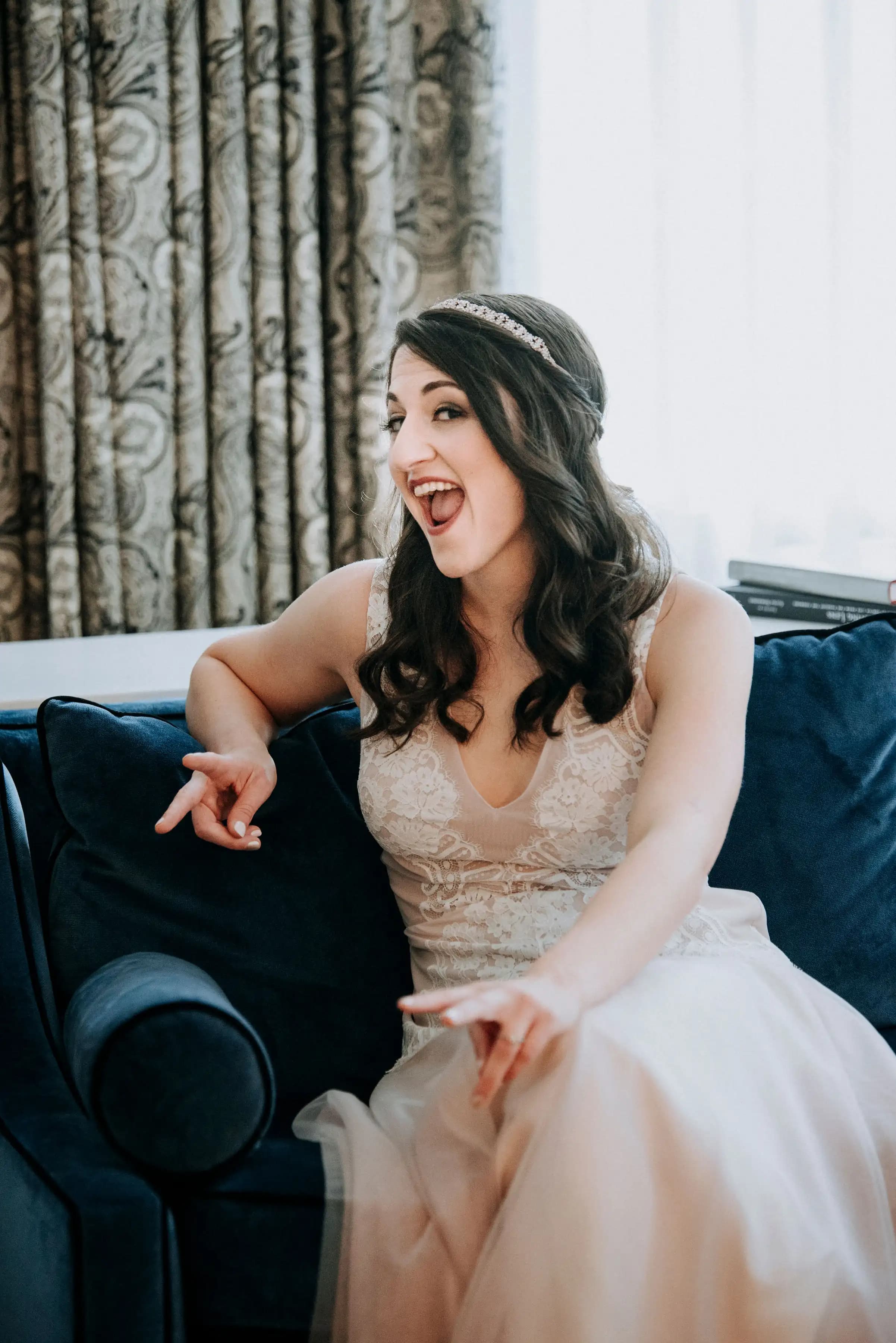 Smiling bride seated on a sofa in a lace gown.