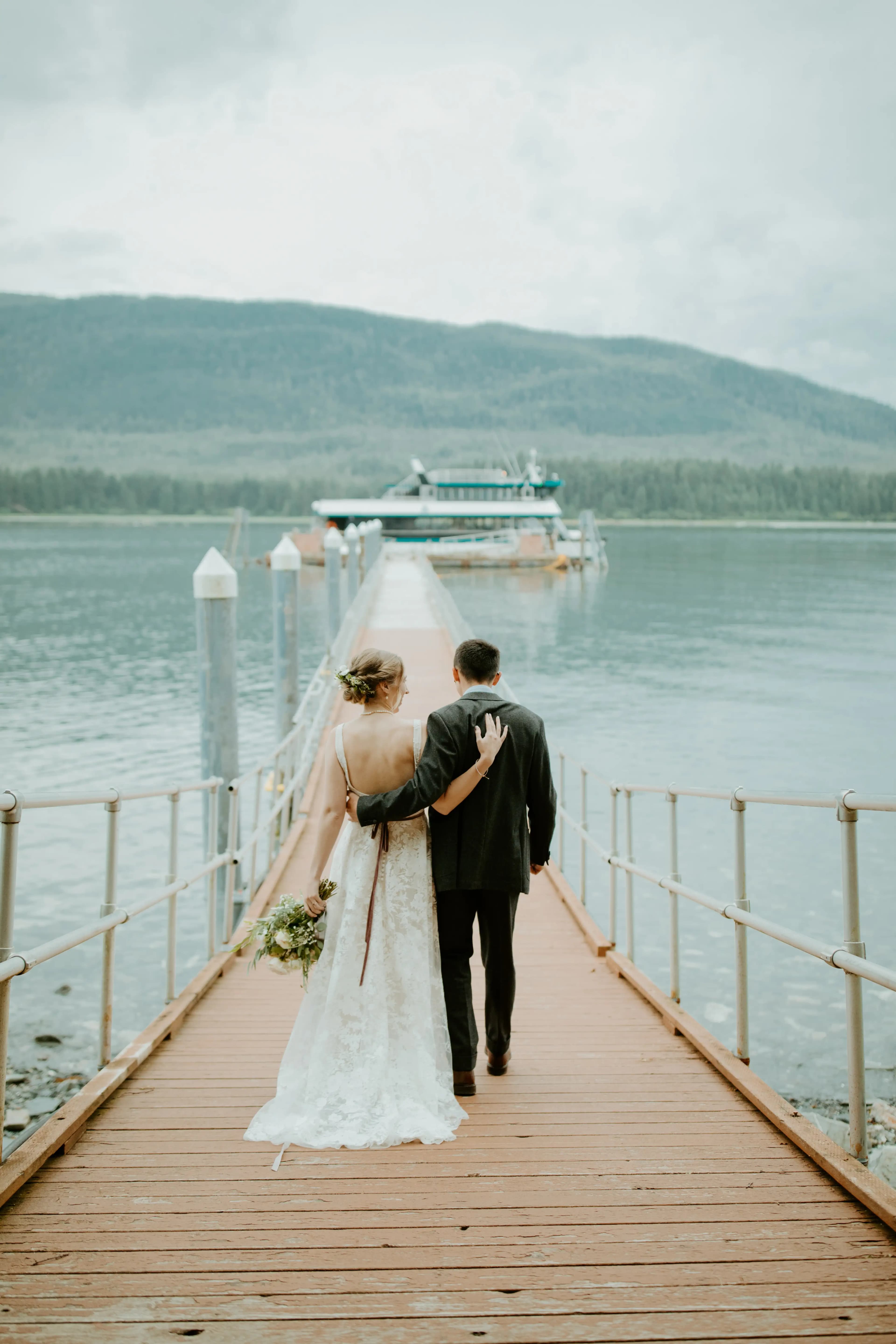 Bride and groom walking down a dock toward a boat.