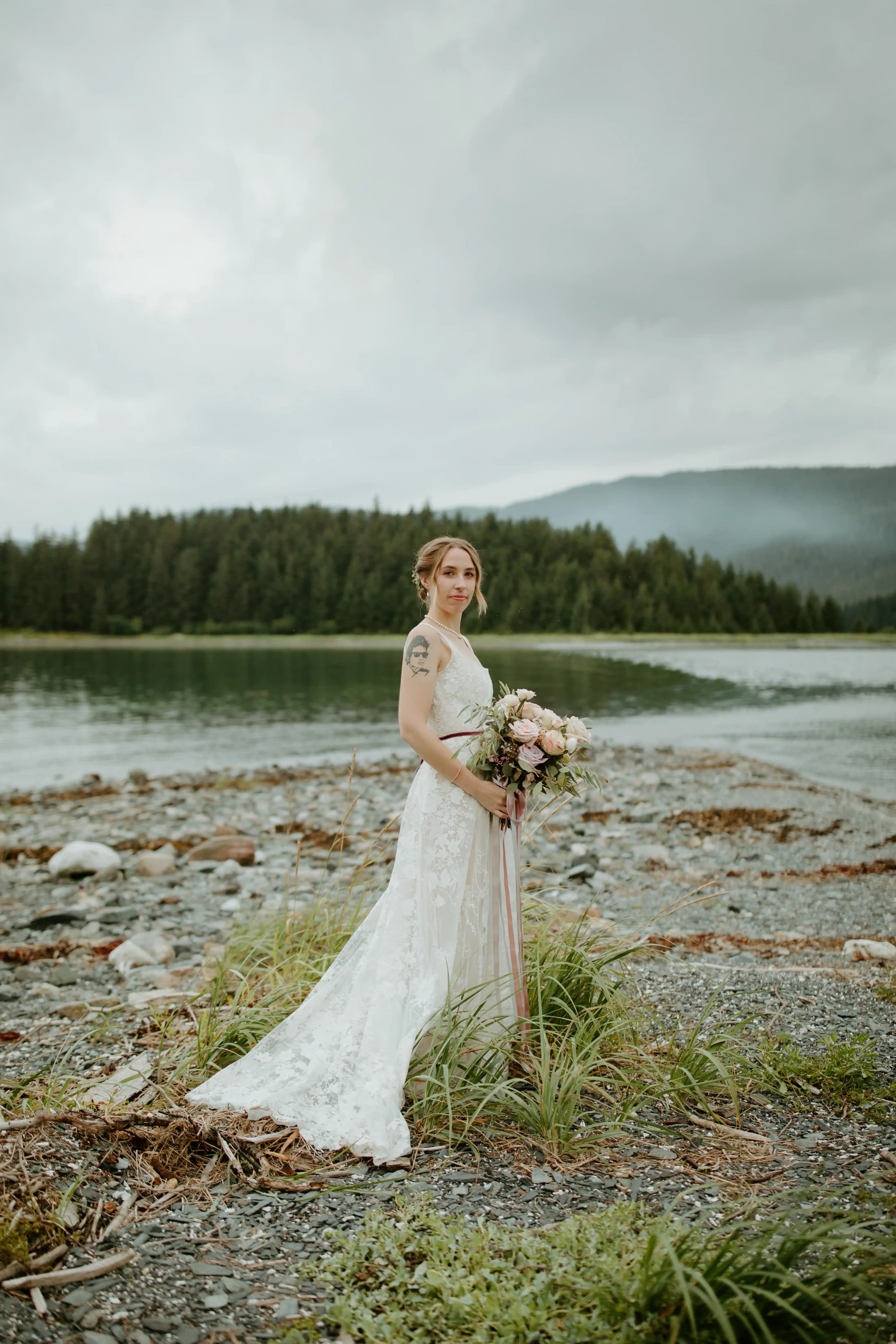 Bride holding a bouquet beside a lake and mountain range.