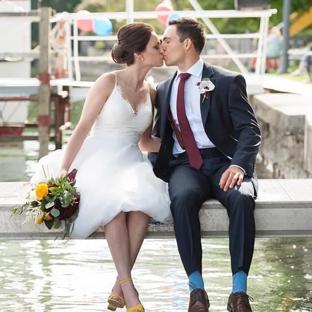 Bride and groom kissing while seated on a dock.