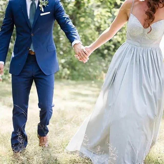 Bride and groom holding hands while walking through a field.
