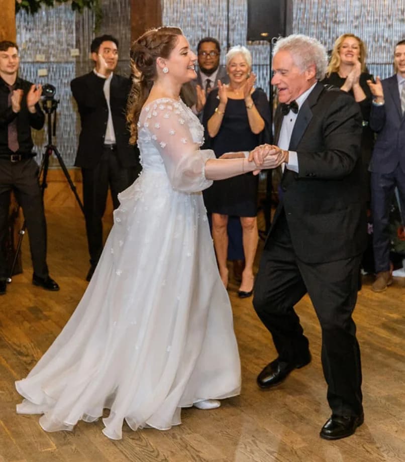 Bride dancing with an older man while guests applaud.