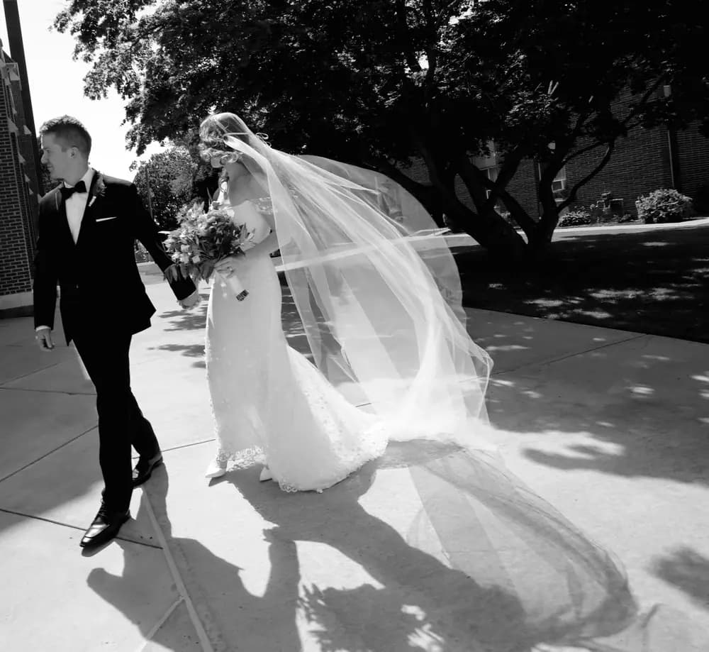 Black-and-white photo of a couple walking with a long veil.