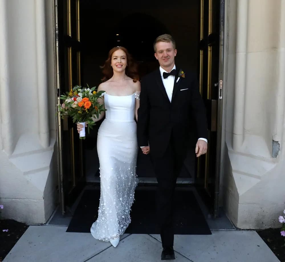 Bride and groom holding hands in a grand doorway.