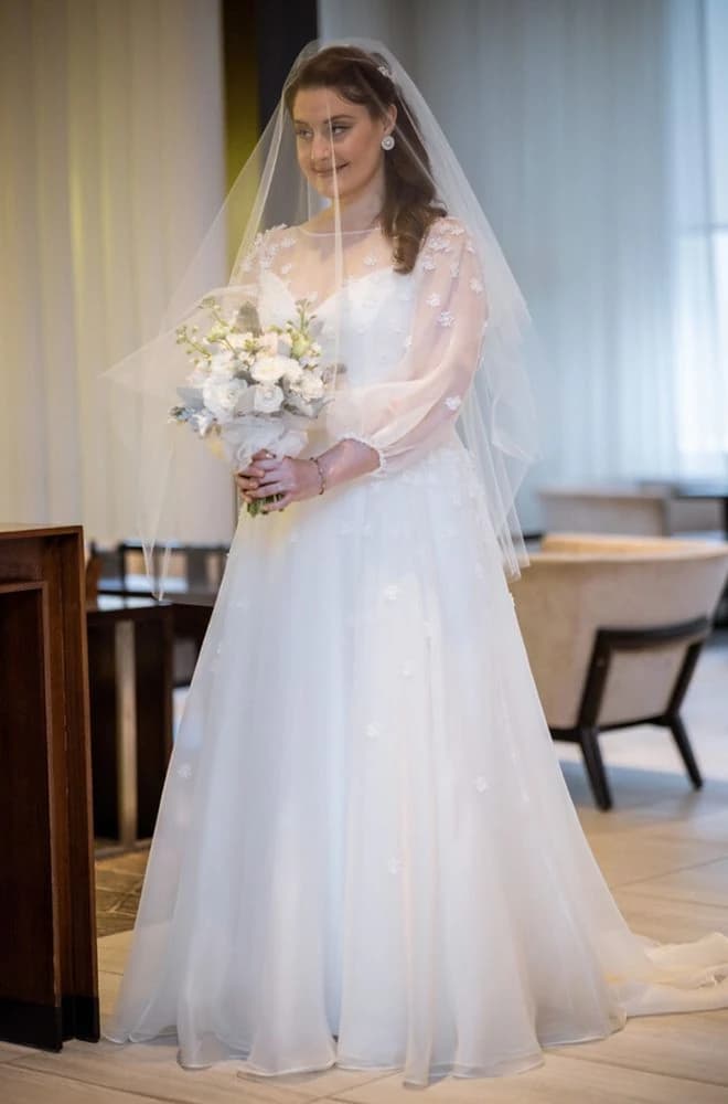Veiled bride holding a white bouquet inside a bright room.