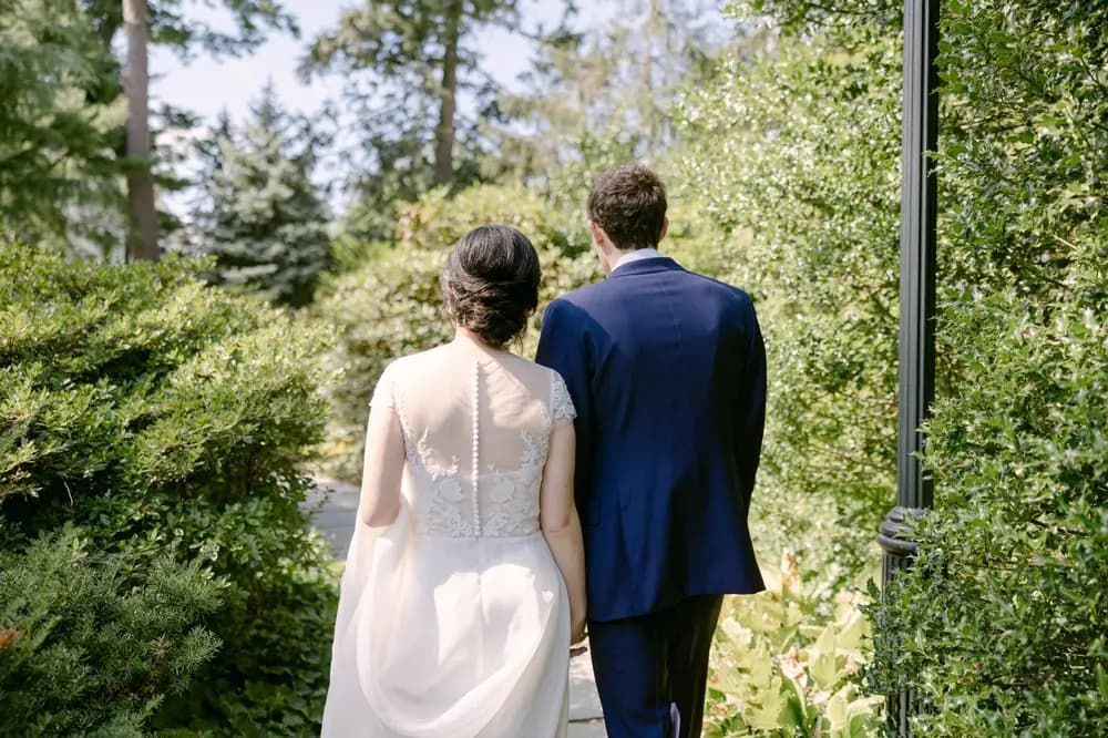 Bride and groom walking away through a garden path.