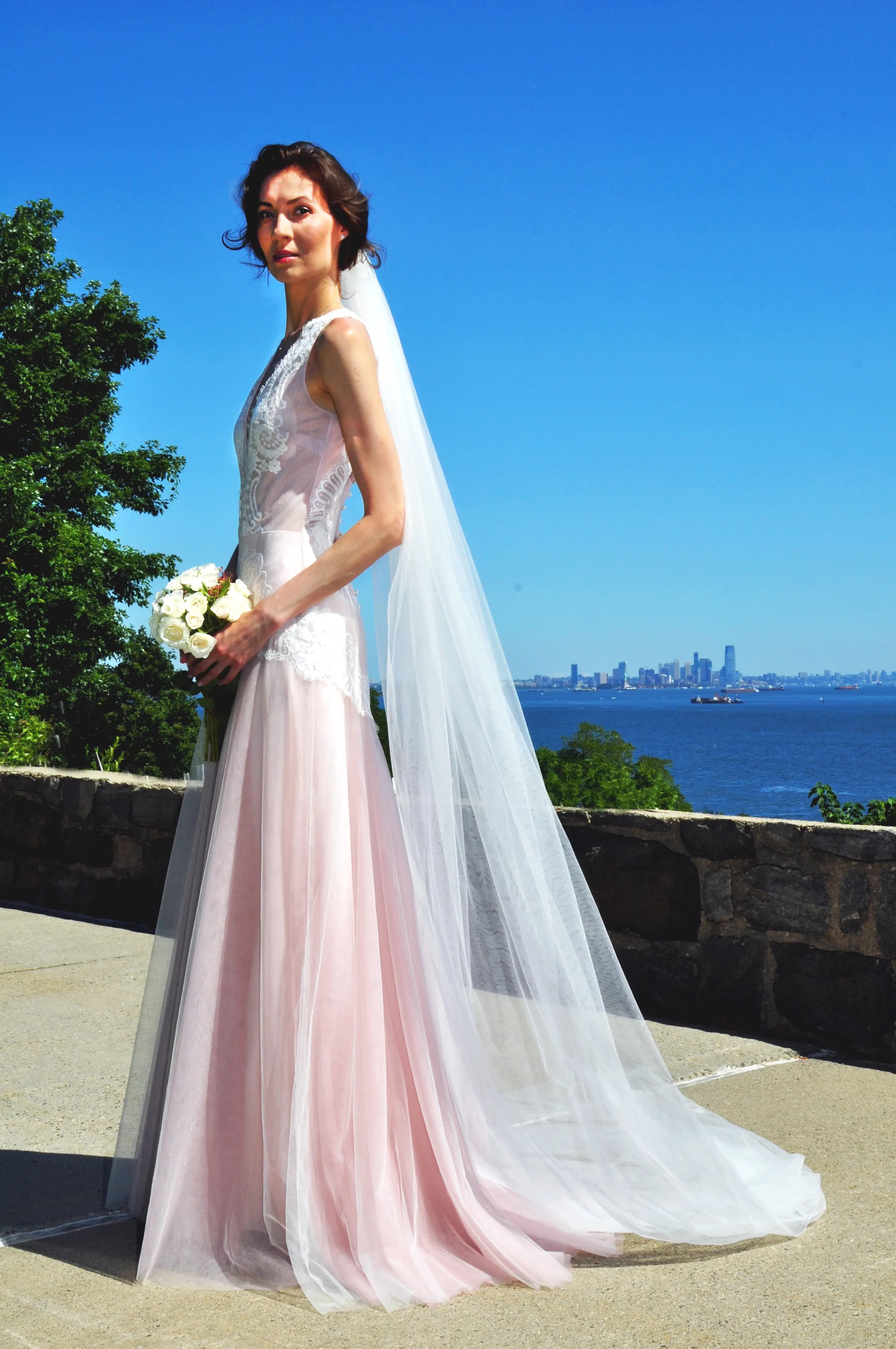 Bride in a sheer lace gown and veil with the skyline behind her.