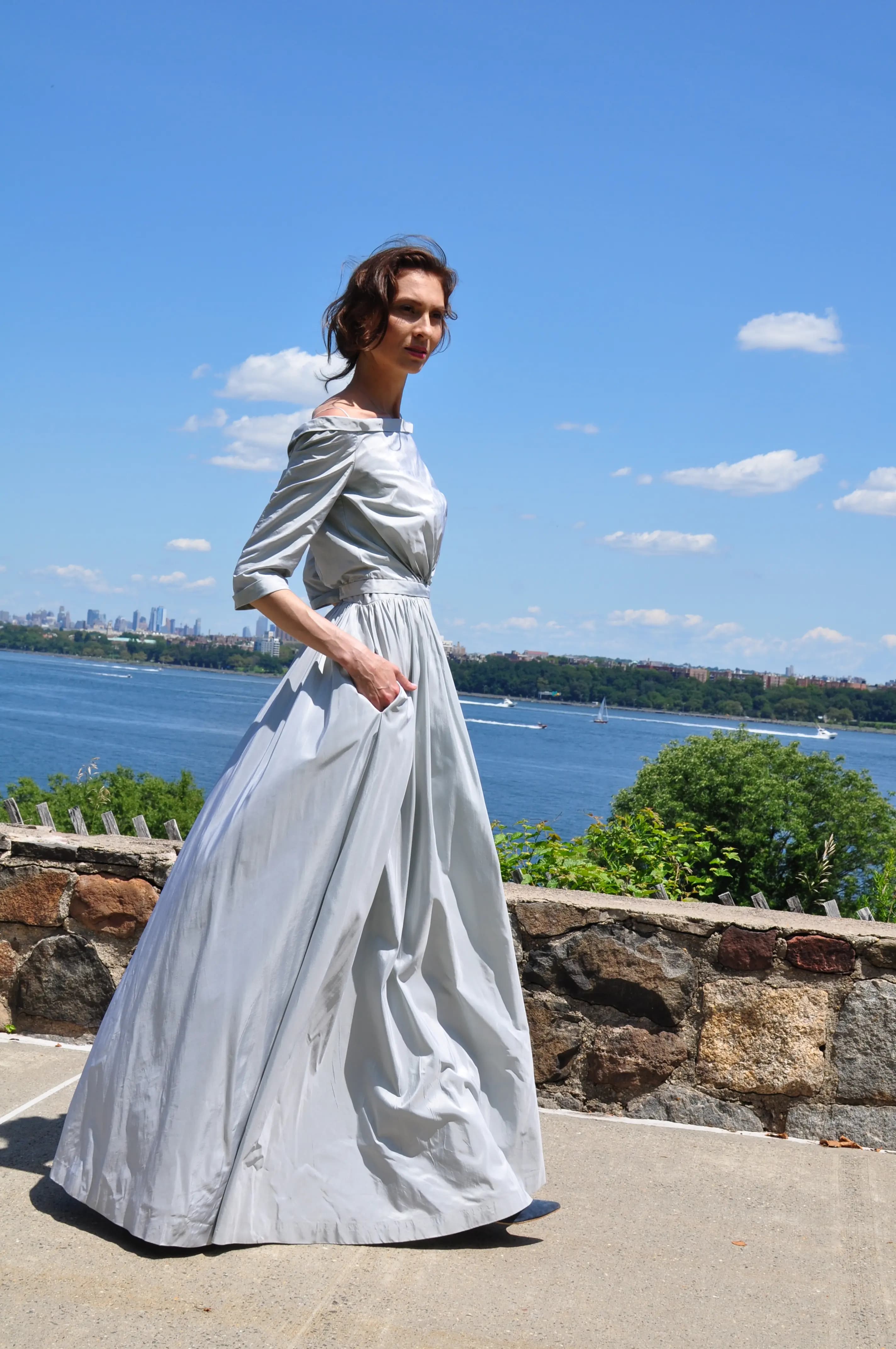 Bride in a draped silver gown beside the water.