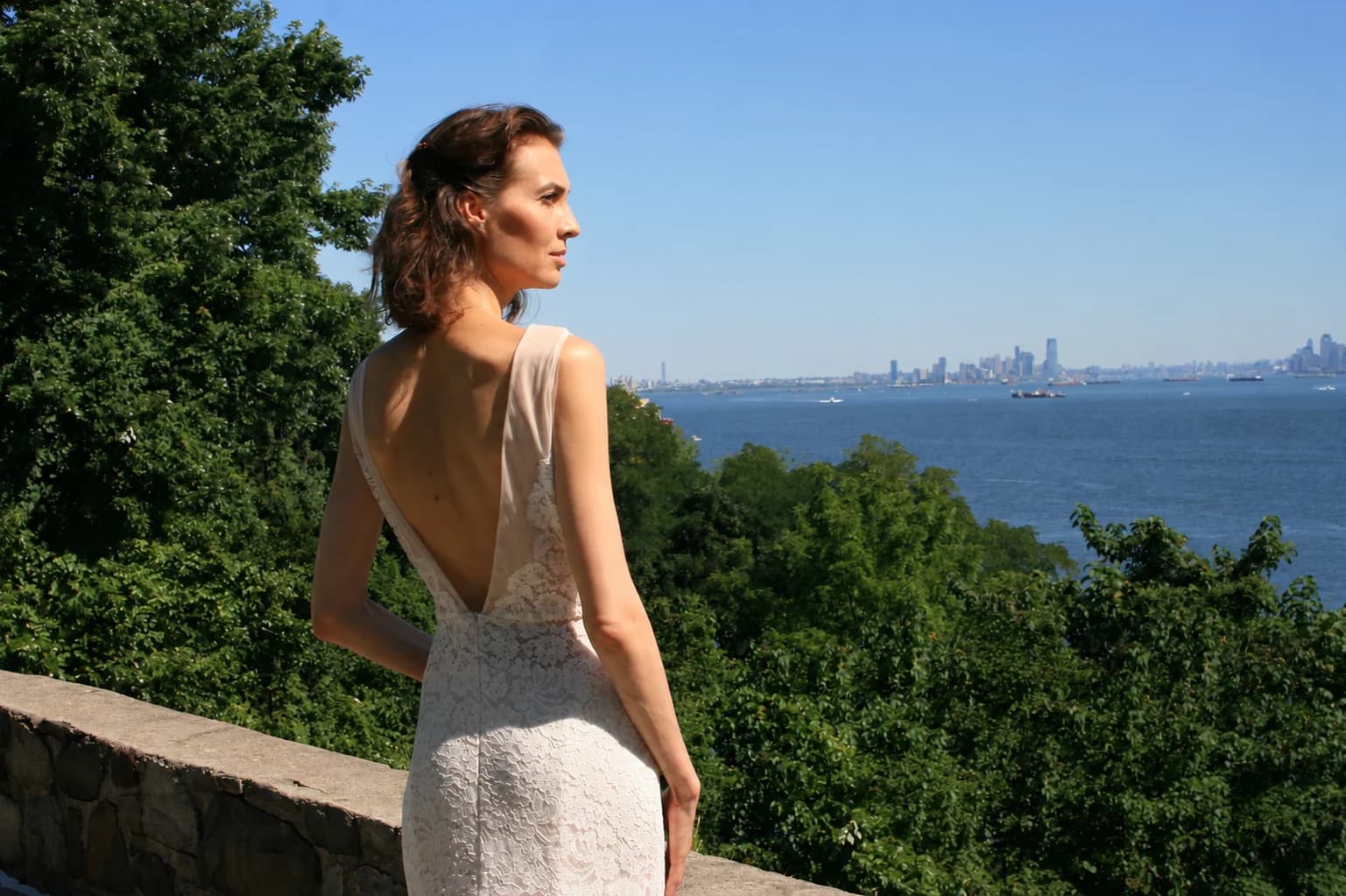Bride showing the open back of a lace gown beside the water.