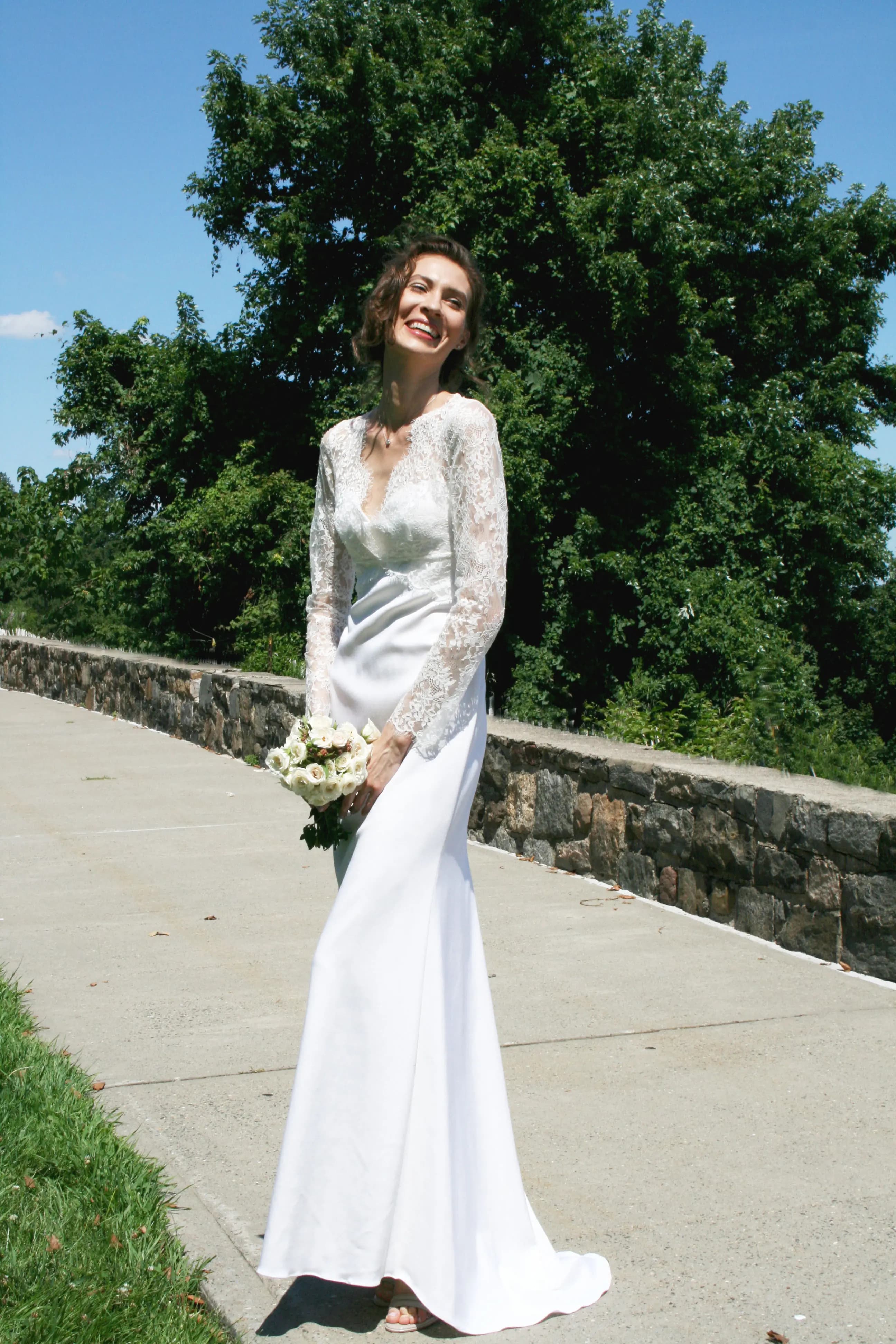 Smiling bride in a lace gown on a garden path.