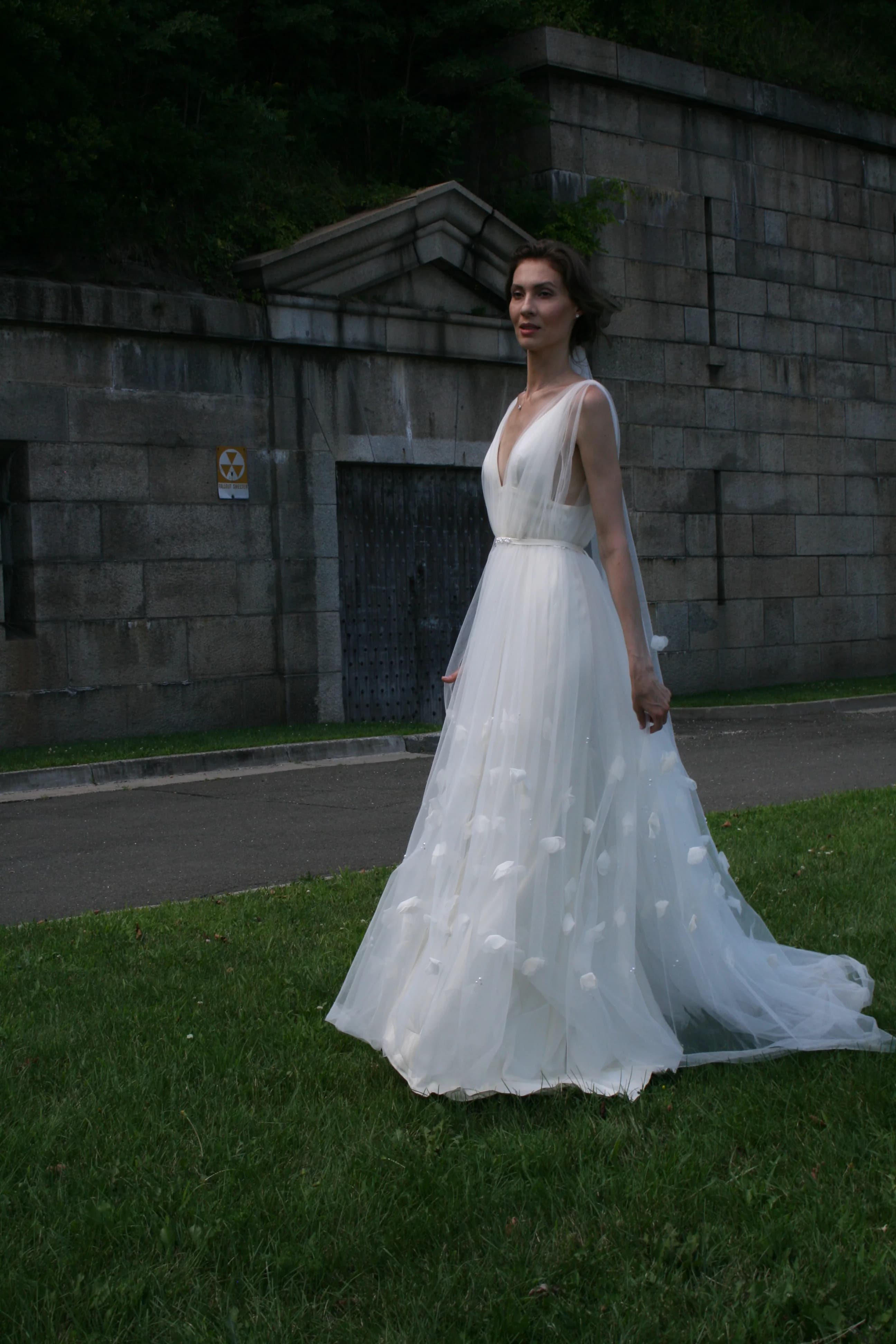 Bride in a flowing gown beside a stone wall.