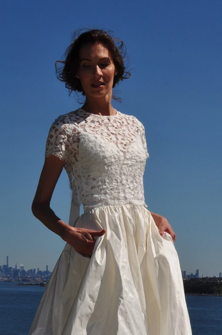 Bride in a lace bodice with the city skyline across the water.