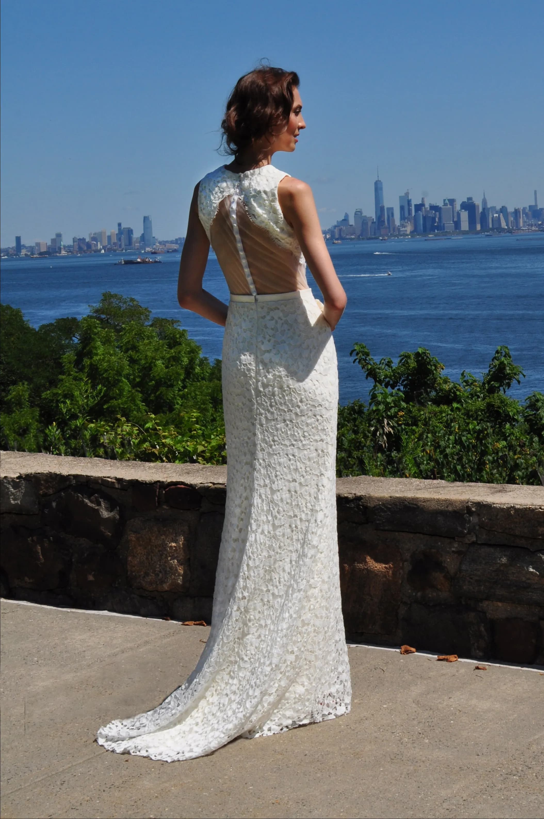 Bride showing the lace back of a gown with the city skyline behind her.