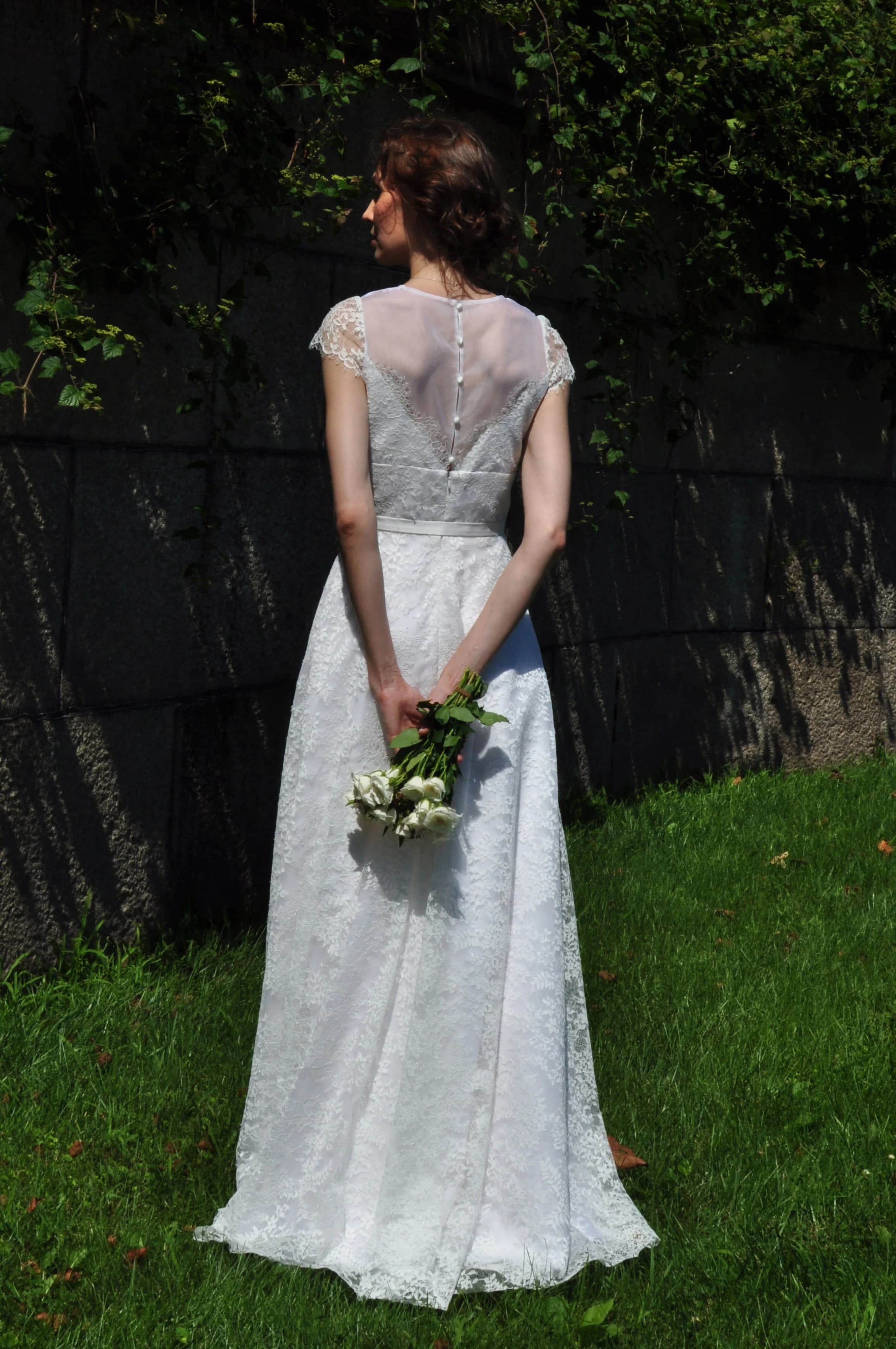 Bride viewed from behind holding white roses in a garden.
