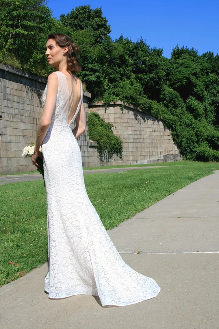 Bride showing the lace back of a gown beside a garden wall.